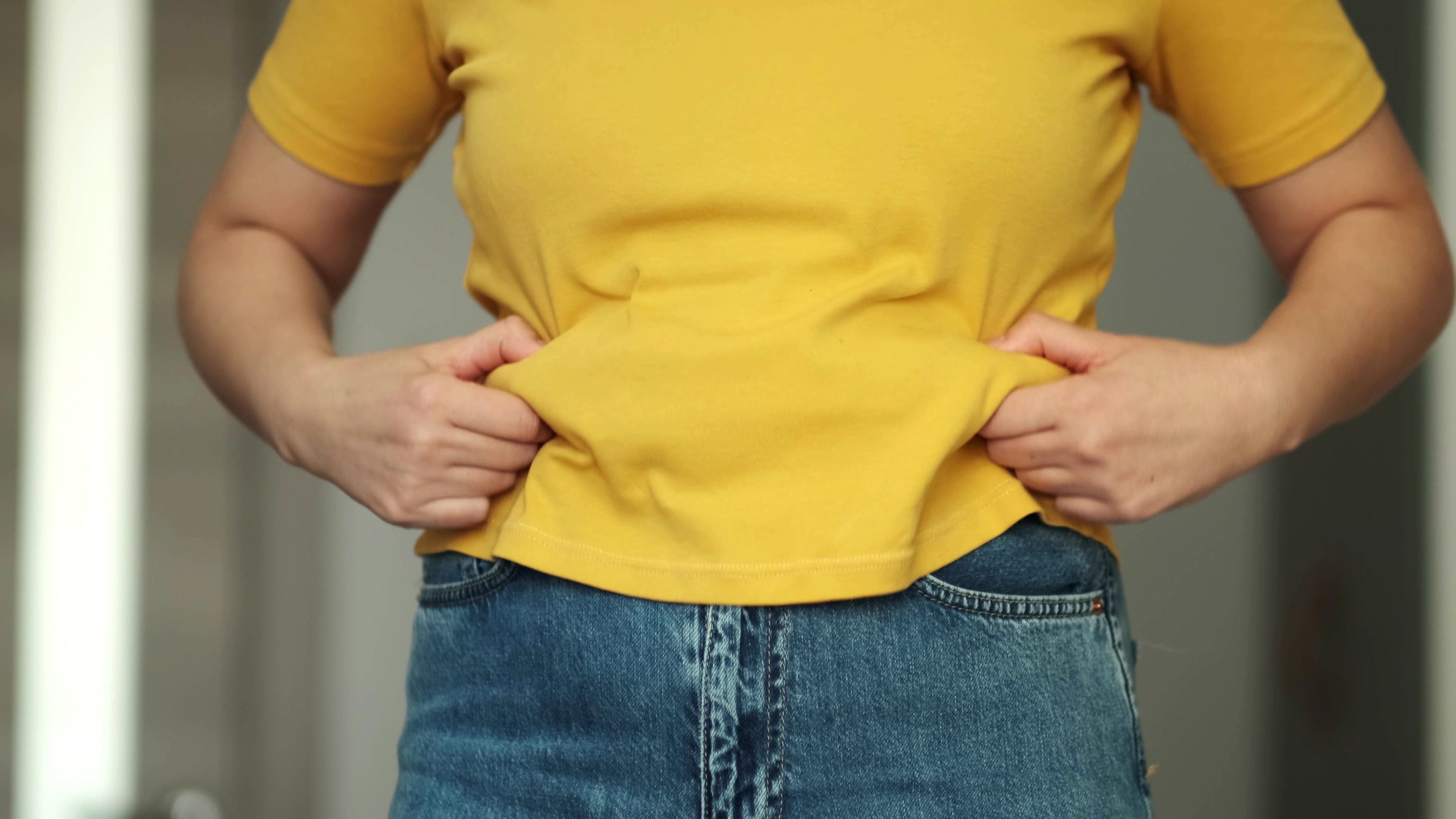 Person in yellow shirt holding belly fat — representing the challenge of losing stubborn belly fat
